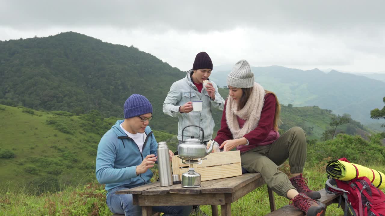 一群亚洲朋友一起在山上露营，坐在户外椅子上喝着热咖啡视频素材