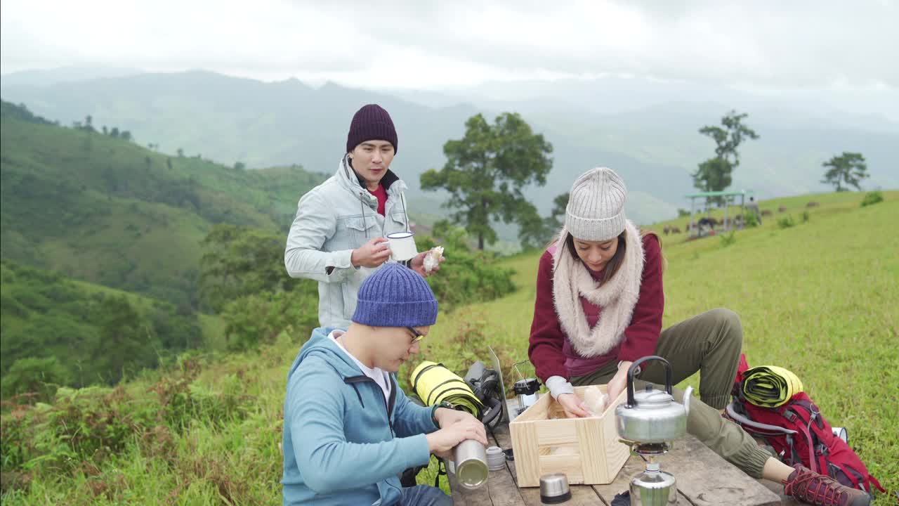 一群亚洲朋友一起在山上露营，坐在户外椅子上喝着热咖啡视频素材