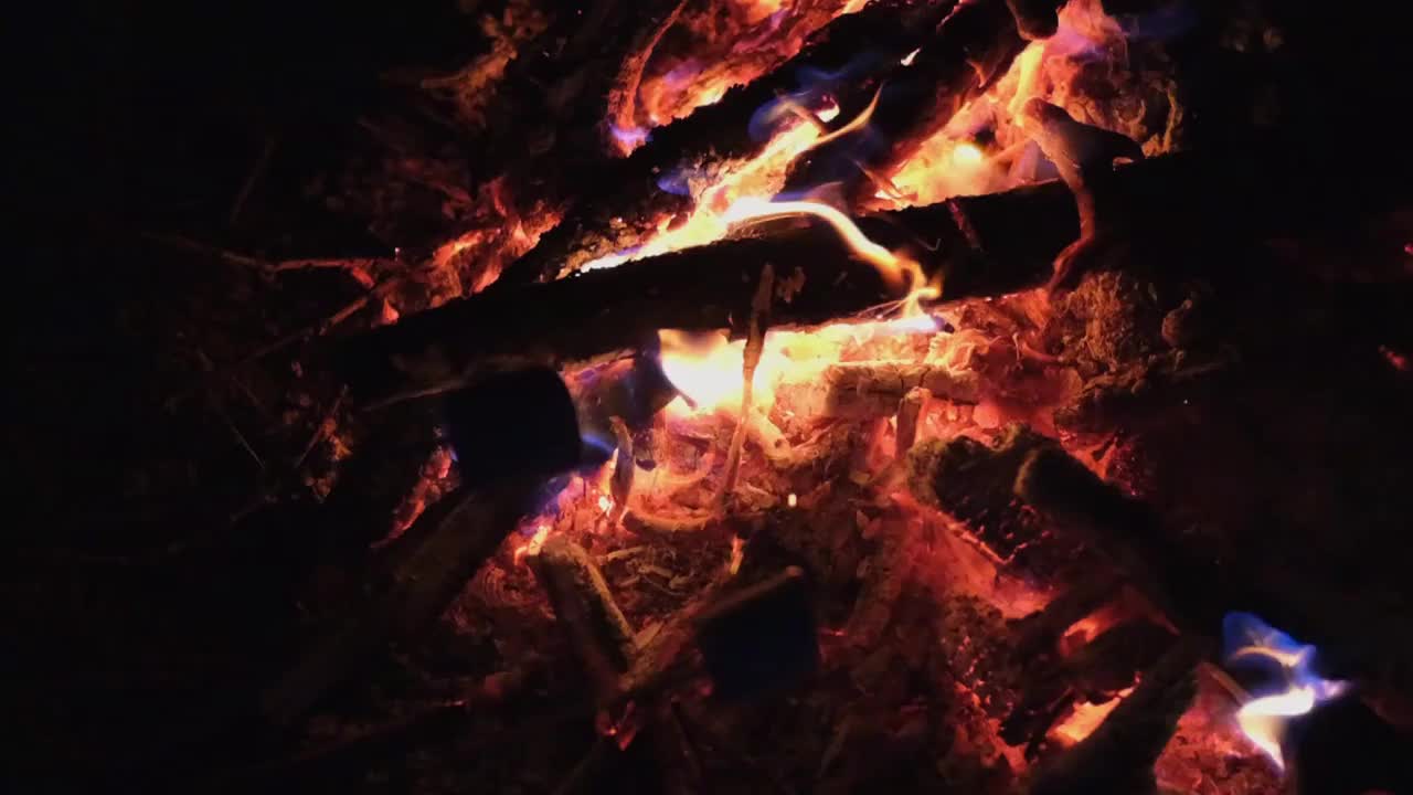 夜晚的篝火特写，木头在燃烧。人们用火煮棉花糖，慢镜头。视频素材