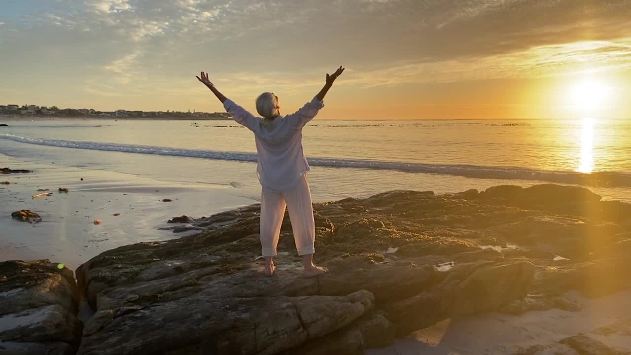 年长的女人在海滩上独自向太阳致敬视频素材