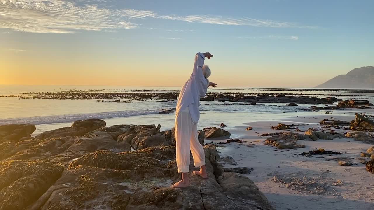 年长的女人在海滩上独自向太阳致敬视频素材