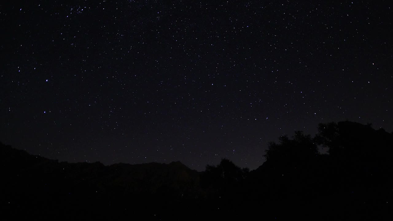 夜空中移动的恒星轨迹的时间间隔。在前景中有一座山顶的银河系的星星。夜晚天空自然夏季景观。英仙座流星雨观测。视频素材