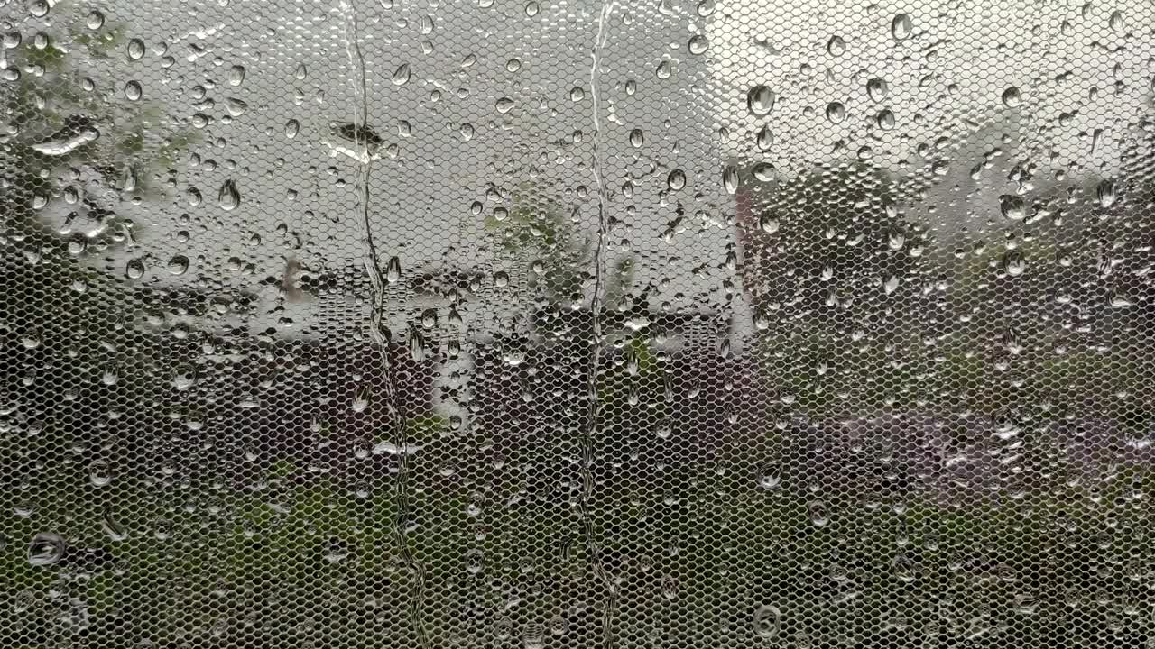 真正的雨滴滑在家庭窗户玻璃上。大雨。玻璃上水滴的特写。视频素材