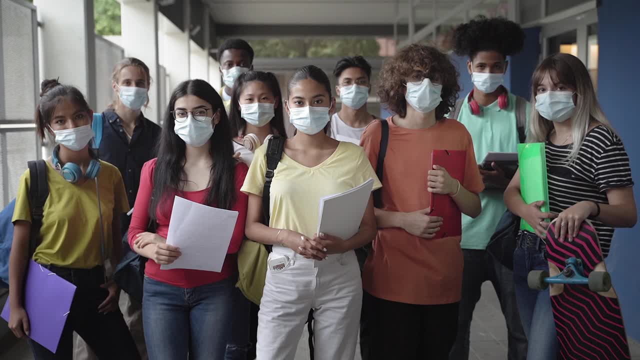 多种族中学生戴上防护口罩站在学校入口处。不同种族的青少年朋友在冠状病毒大流行期间回到高中视频素材