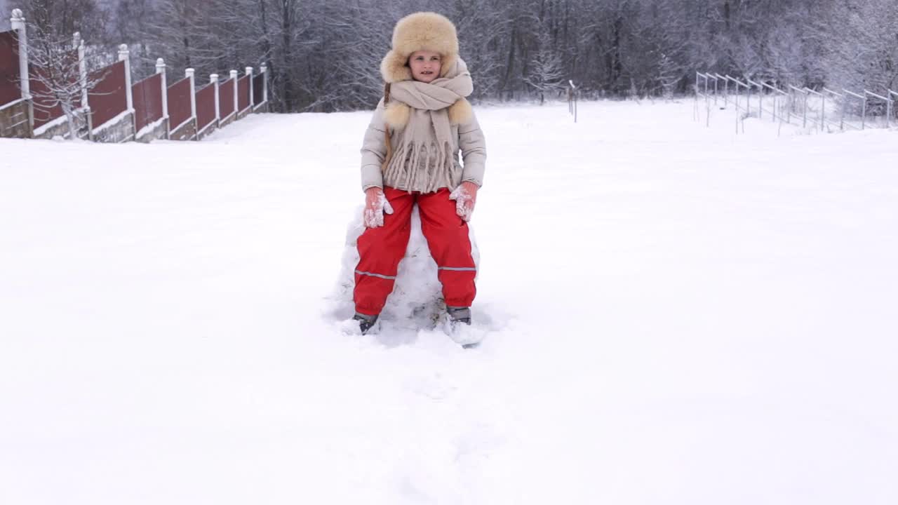 一个学龄前的小女孩坐在雪地里玩雪。下雪的冬天，周末，乐趣。视频素材