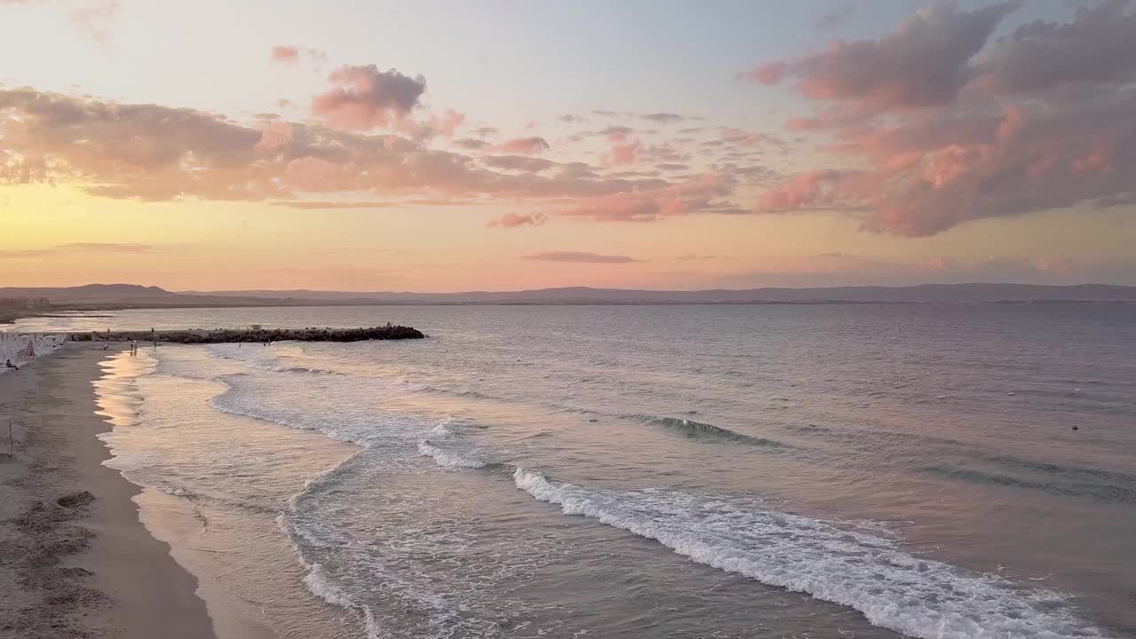 鸟瞰图与蓝色的海浪下的紫色日落天空。视频素材