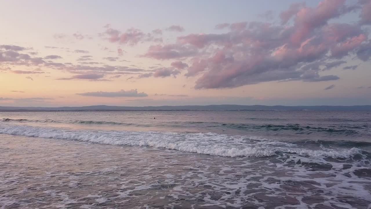 鸟瞰图与蓝色的海浪下的紫色日落天空。视频素材