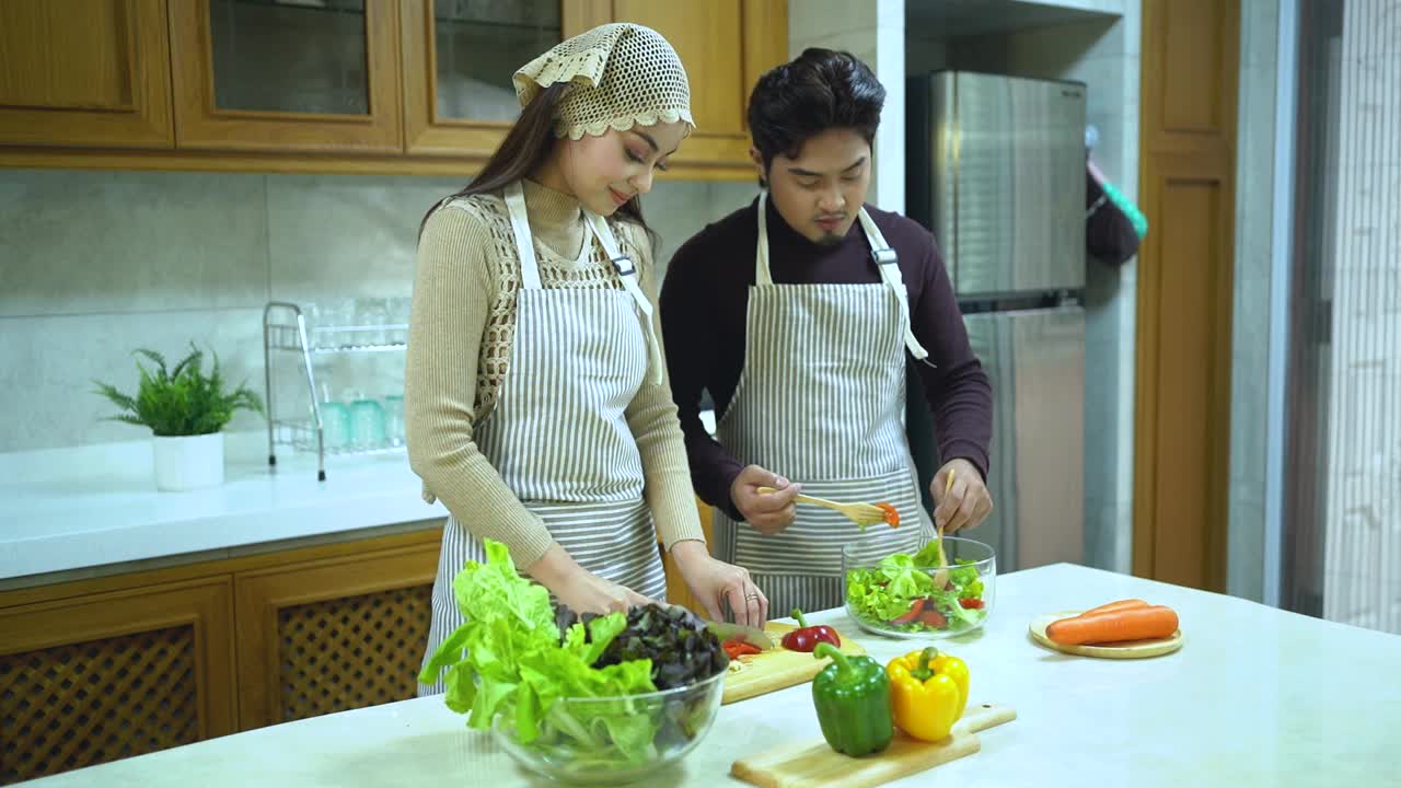 亚洲夫妇一起做饭。夫妻俩在家里的厨房里准备健康的蔬菜食品。视频素材