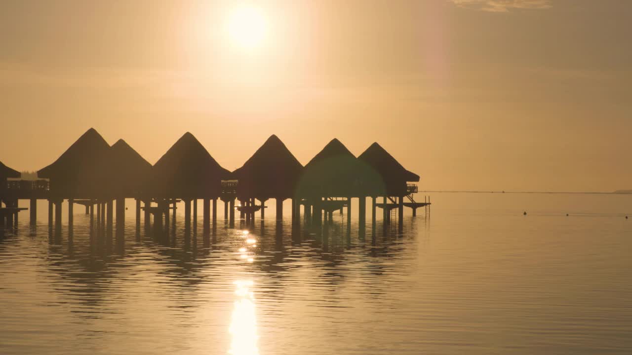 度假酒店在旅游度假天堂的日落海滩与水上平房在海洋泻湖与珊瑚礁海。来自波拉波拉，法属波利尼西亚，塔希提岛，南太平洋的4K视频。视频素材