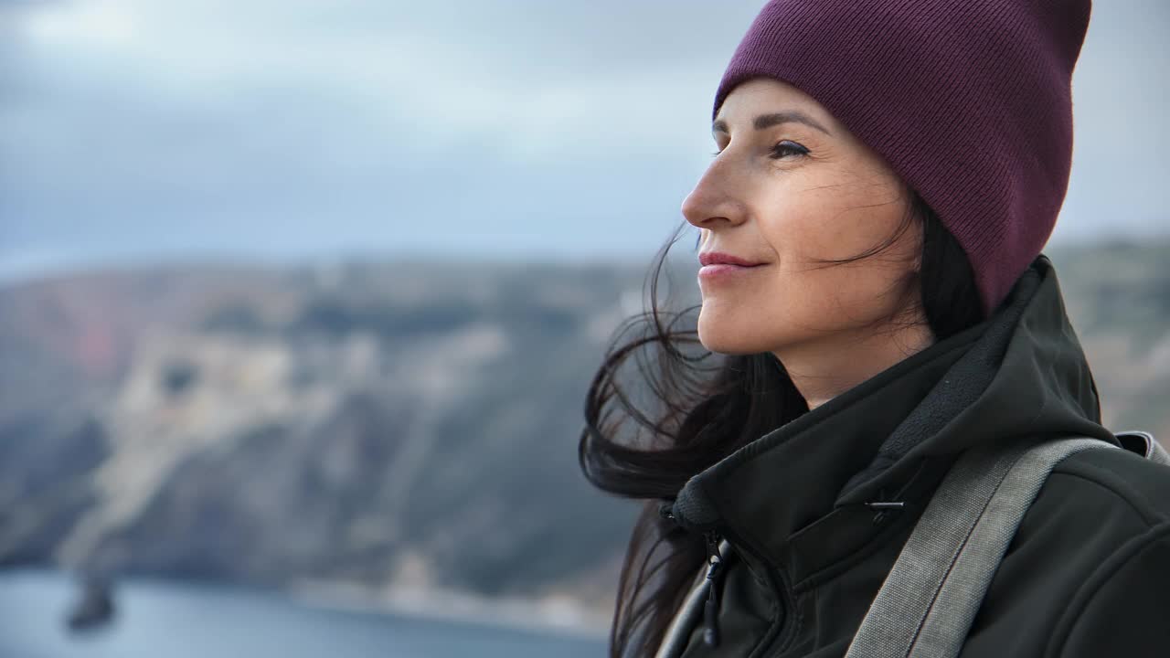 快乐的黑发女子与波浪的头发微笑着欣赏自然风景山顶旅游度假视频素材