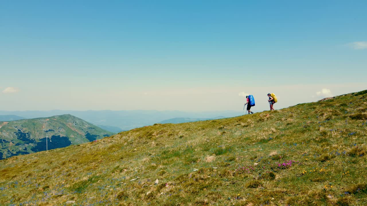 鸟瞰图一对游客从山顶下来。在山里旅行。两个背着蓝色和黄色双肩包的徒步旅行者在山上视频素材