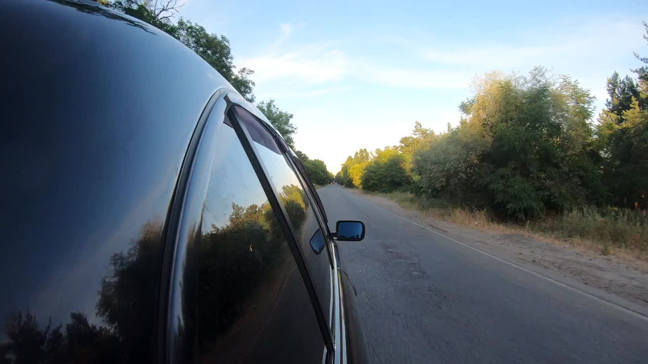 黑色汽车沿着公路行驶，穿过美丽的风景。夏日高速公路上行驶的汽车侧面的POV。在乡间道路上行驶的汽车。自驾游的概念。慢动作视频素材