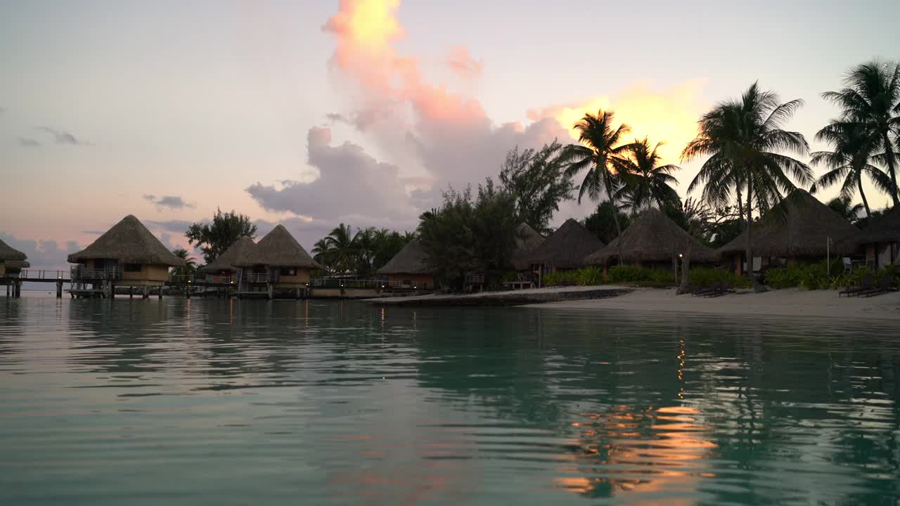 旅游度假天堂日落海滩与海滩水上平房度假村酒店在珊瑚礁泻湖海。来自波拉波拉，法属波利尼西亚，塔希提岛，南太平洋的4K视频。视频素材