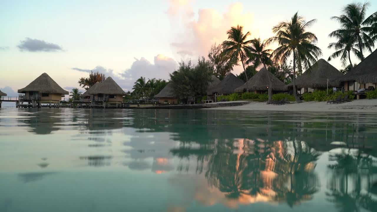 度假酒店在旅游度假天堂日落海滩与海滩上的平房在海洋泻湖与珊瑚礁海。来自波拉波拉，法属波利尼西亚，塔希提岛，南太平洋的4K视频。视频素材