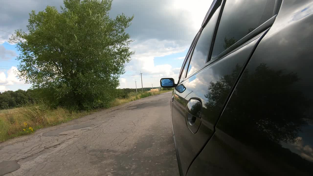 从行驶在乡村公路上的汽车一侧的观点。驾车穿越美丽的风景。夏天的一天，一辆黑色轿车在马路上行驶。自驾游的概念。慢动作视频素材