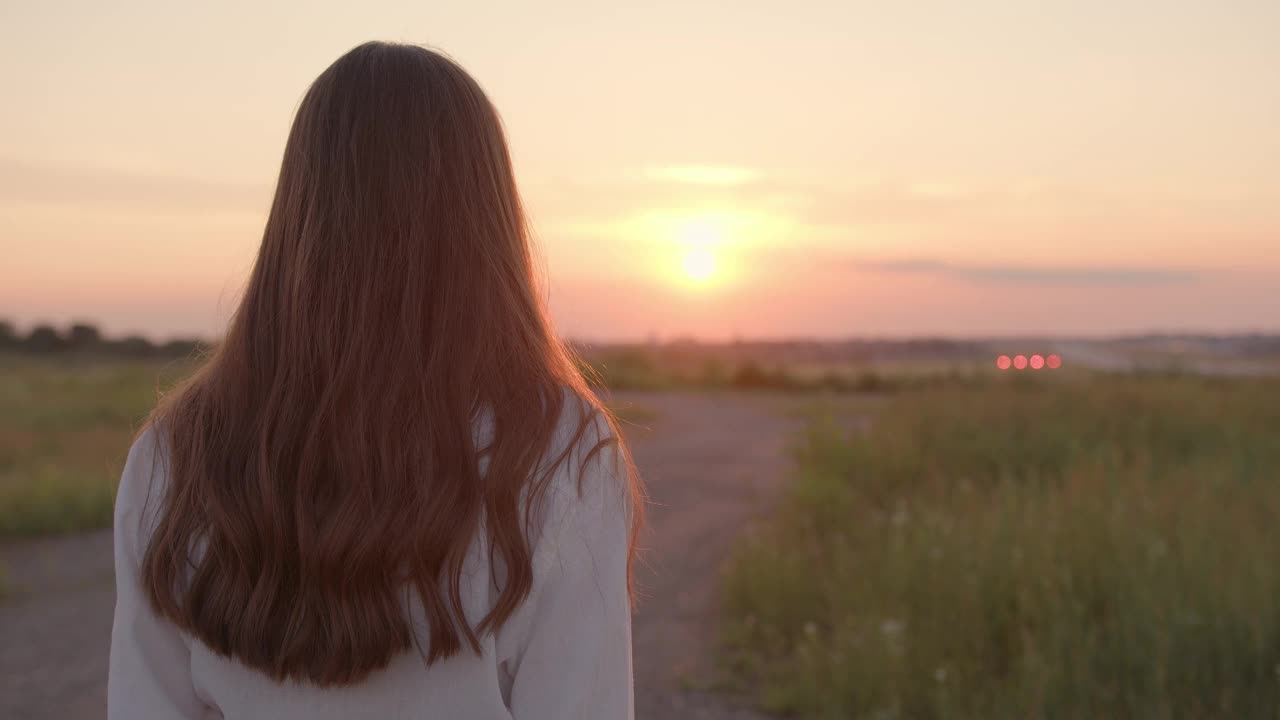 一个女人走在田野上，抚摸着她卷曲的棕色头发视频素材