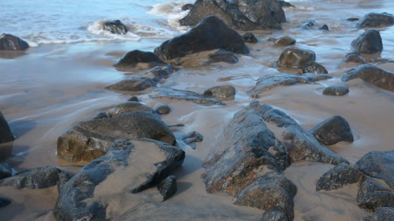 海浪拍打着海滩上的岩石，一个人在走。视频下载