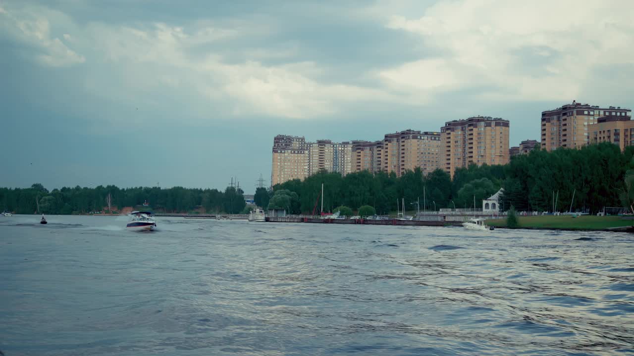 一艘游艇在阴天驶过河。城市是背景视频素材