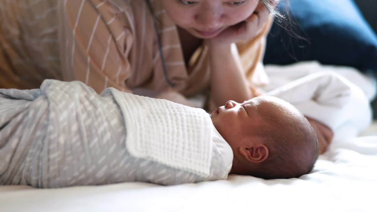 亚洲母亲看着她熟睡的新生婴儿在床上视频素材