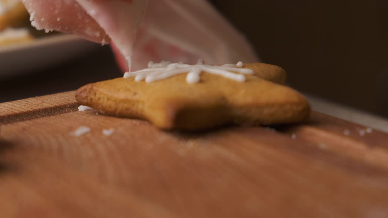 靠近的女人手装饰圣诞姜饼的形状与冰霜在木制的桌子上。为假期做准备。视频素材