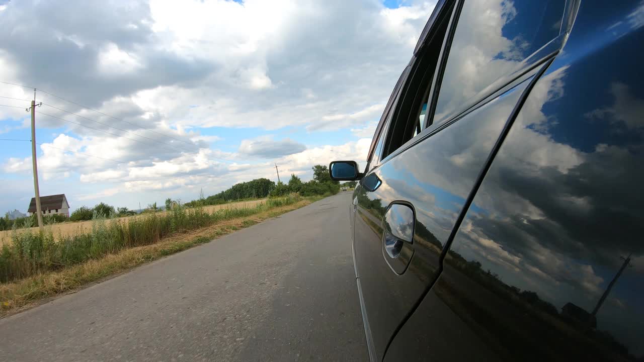 从行驶在乡村公路上的汽车一侧的观点。驾车穿越美丽的风景。夏天的一天，一辆黑色轿车在马路上行驶。自驾游的概念。慢动作视频素材