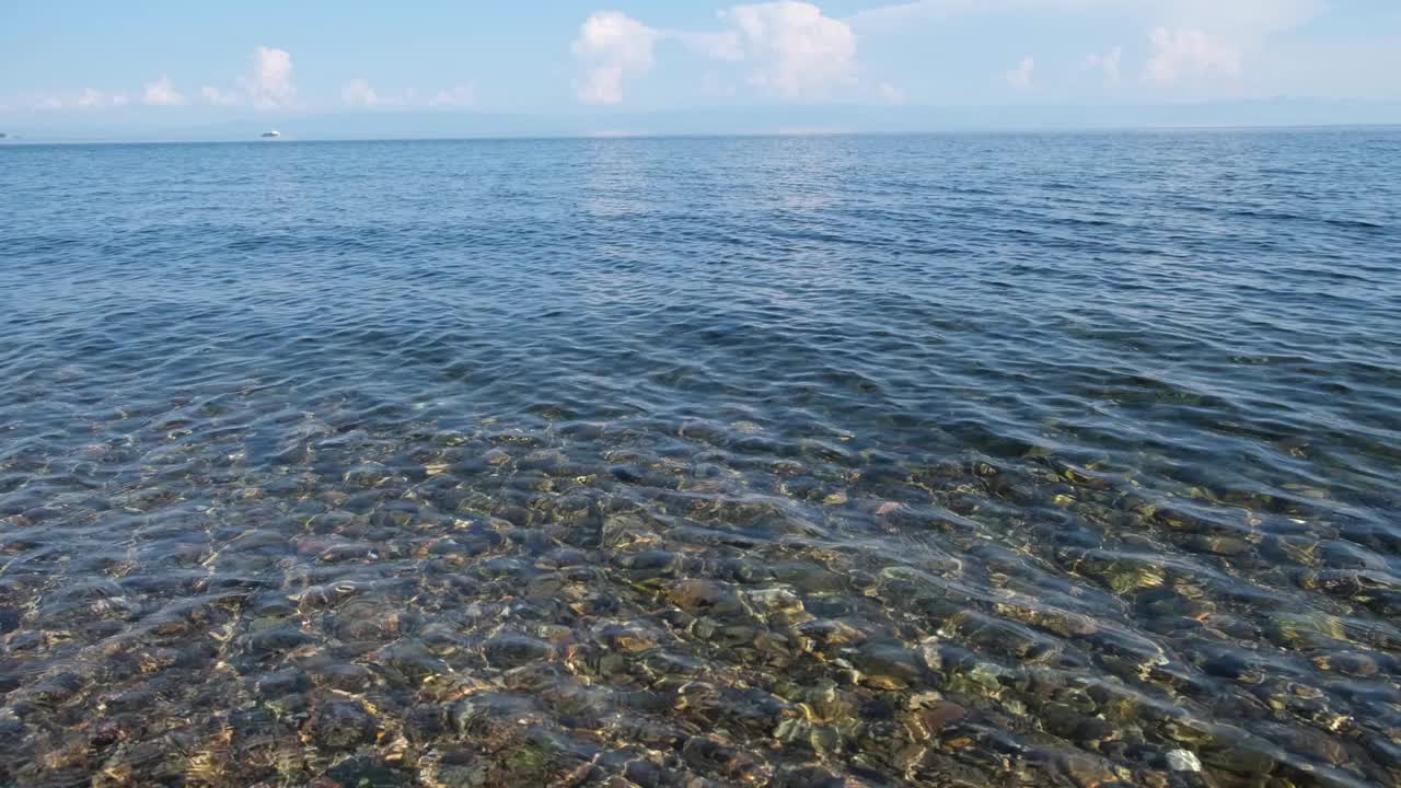 鹅卵石湖床透过清澈的波纹湖贝加尔湖透明的水自然背景与白色的船视频素材