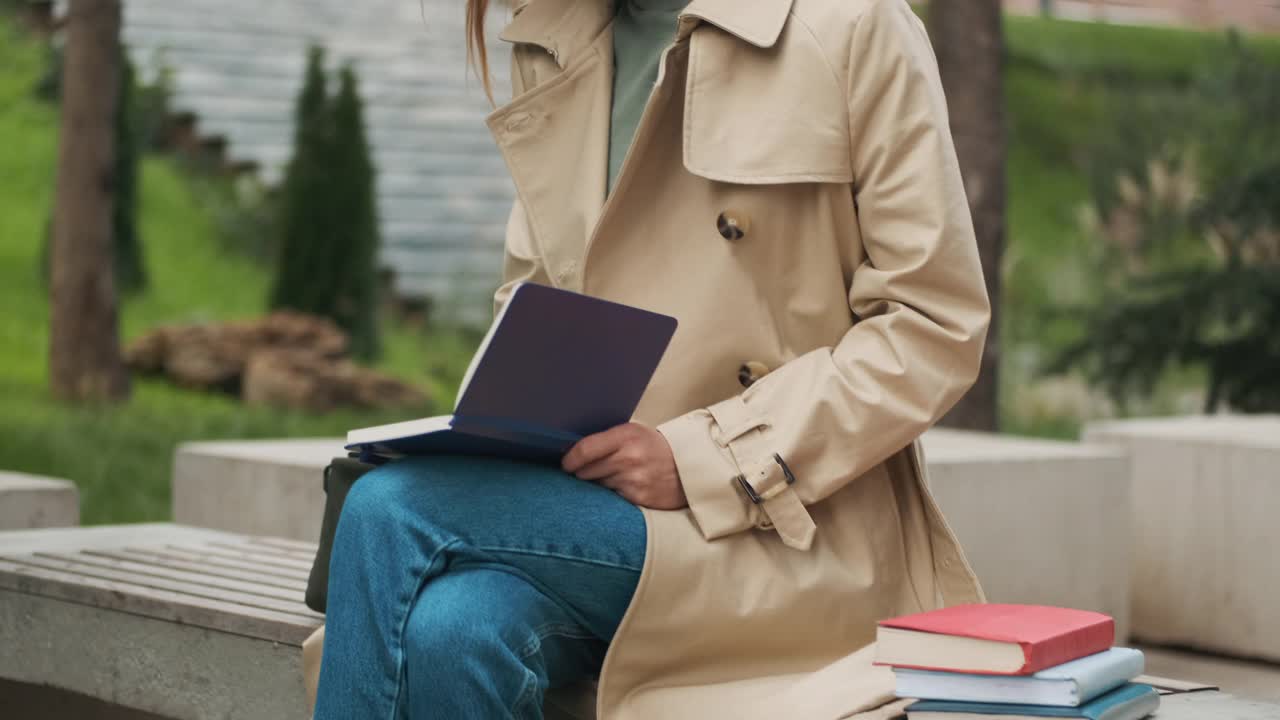 美丽的女学生拿着书在公园的长椅上学习视频素材