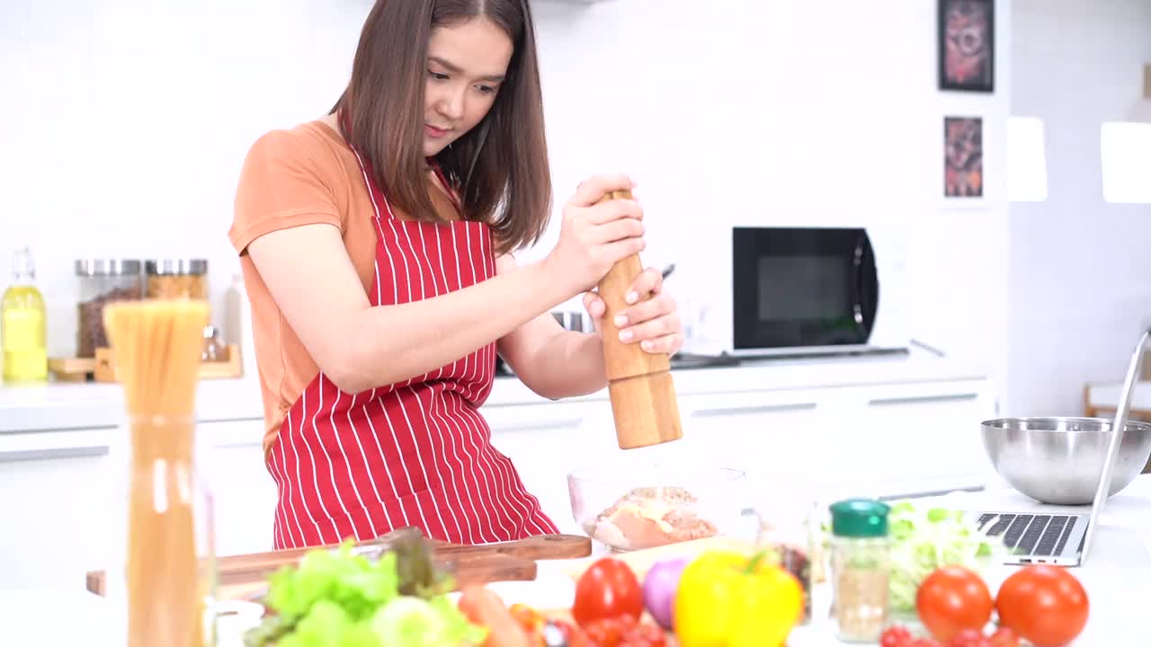 年轻女子研磨胡椒，在炉子上用一个大的胡椒研磨机把胡椒磨成盘子，用来煮肉或蔬菜。年轻的妇女们在厨房里帮忙切蔬菜。视频素材