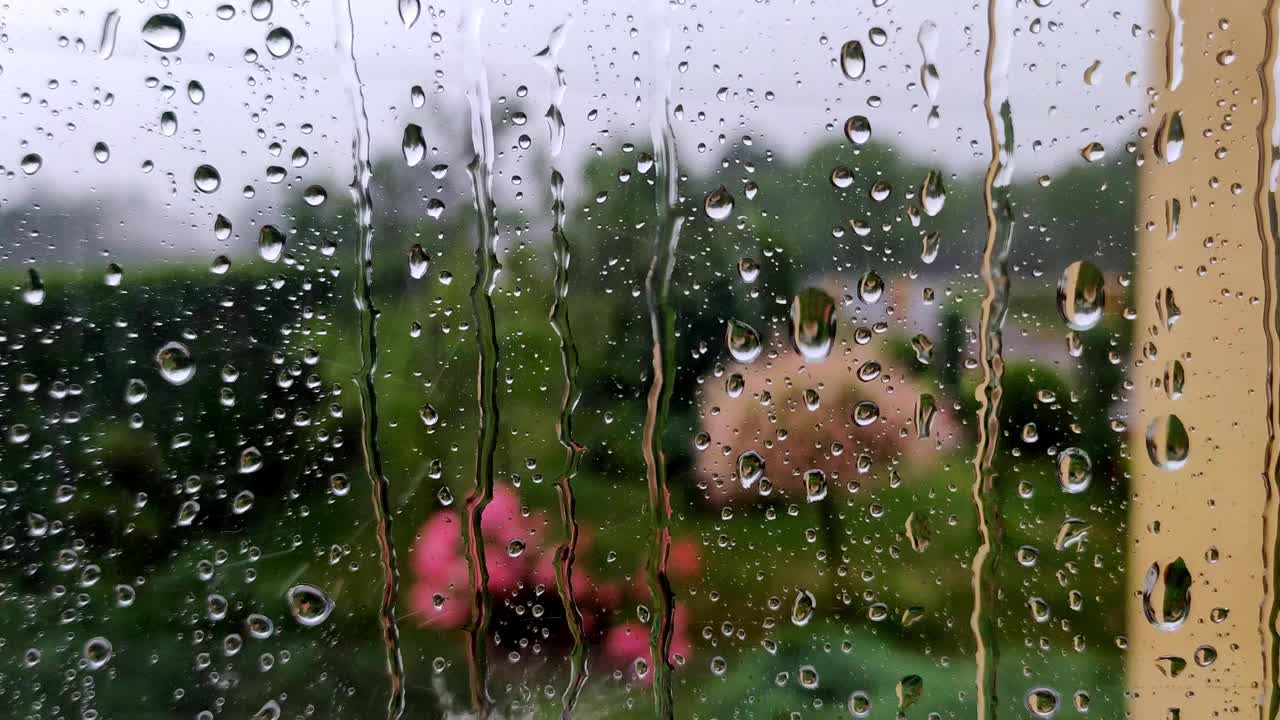 真正的雨滴滑落在家里的窗户玻璃上。大雨。玻璃上水滴的特写镜头。视频素材