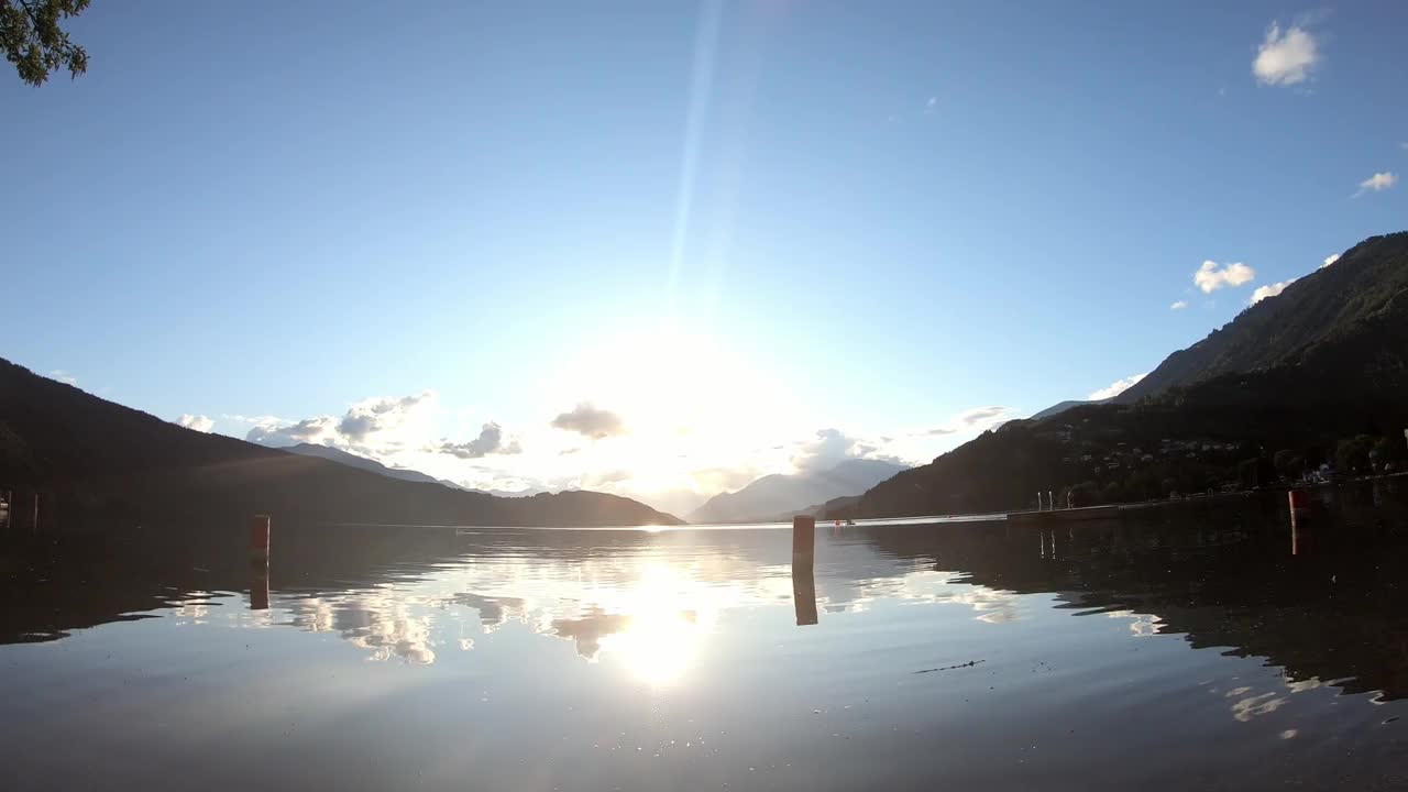 奥地利米尔斯泰特湖畔的日落。太阳正在阿尔卑斯山后面落下。平静的湖面轻轻地波浪起伏。晴朗的天空。湖边的一个小村庄。平静和放松视频素材