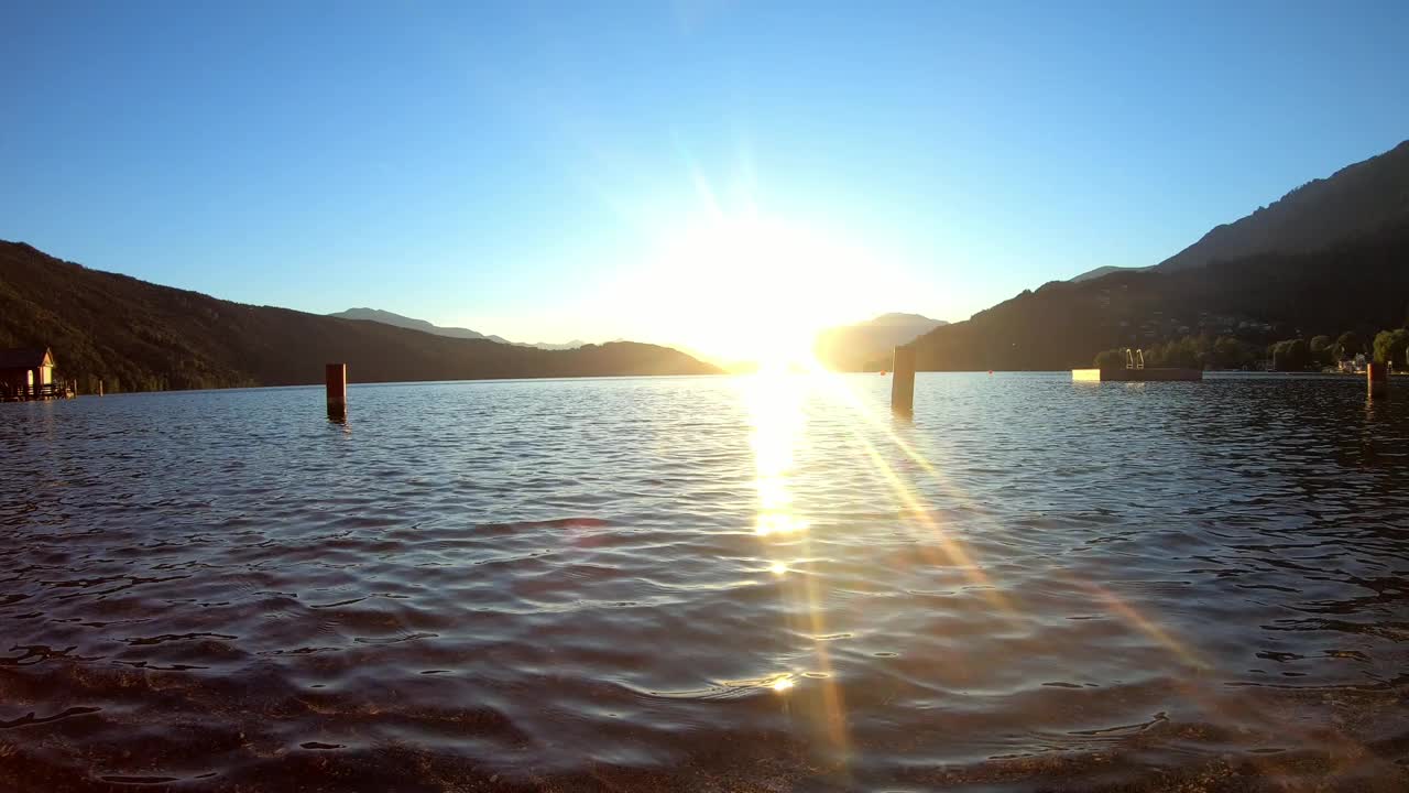 奥地利米尔斯泰特湖畔的日落。太阳正在阿尔卑斯山后面落下。平静的湖面轻轻地波浪起伏。晴朗的天空。湖边的一个小村庄。平静和放松视频素材