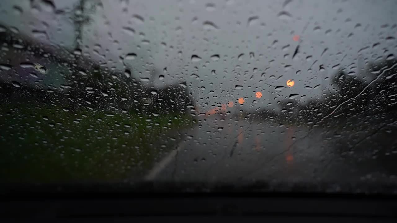雨落在汽车镜子上的运动。在大雨倾盆的城市街道上开车可以缓解夜间的交通堵塞。视频素材