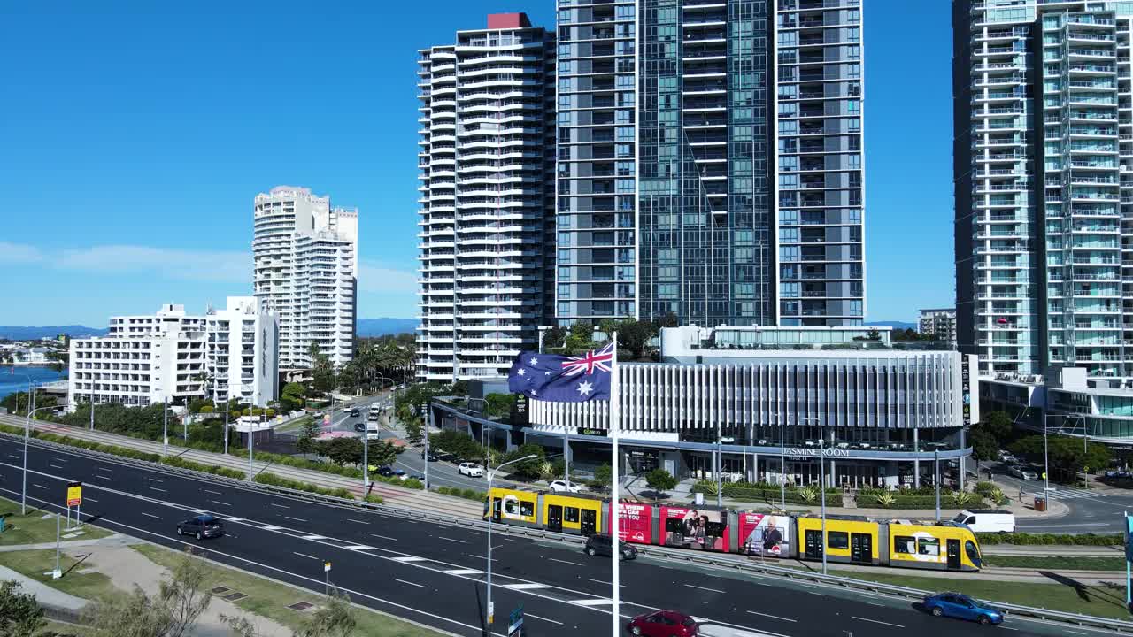 现代电车行驶在城市天际线，一面旗帜在微风中飘扬，背景是高耸的高层建筑。独特的平移无人机视图视频素材