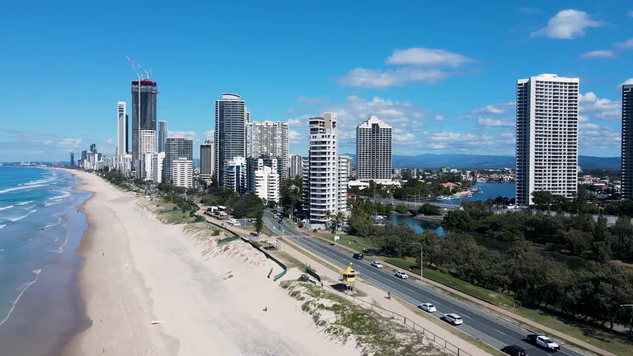 在一个受欢迎的度假小镇，高耸的城市天际线从一段海岸海滩上升起。移动高无人机视图。视频素材