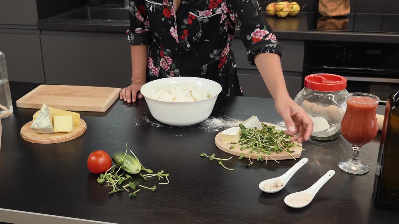 在家为传统披萨准备面团的女性。女人为家人做饭，往碗里加入配料。在现代家庭厨房里制作披萨的过程视频素材