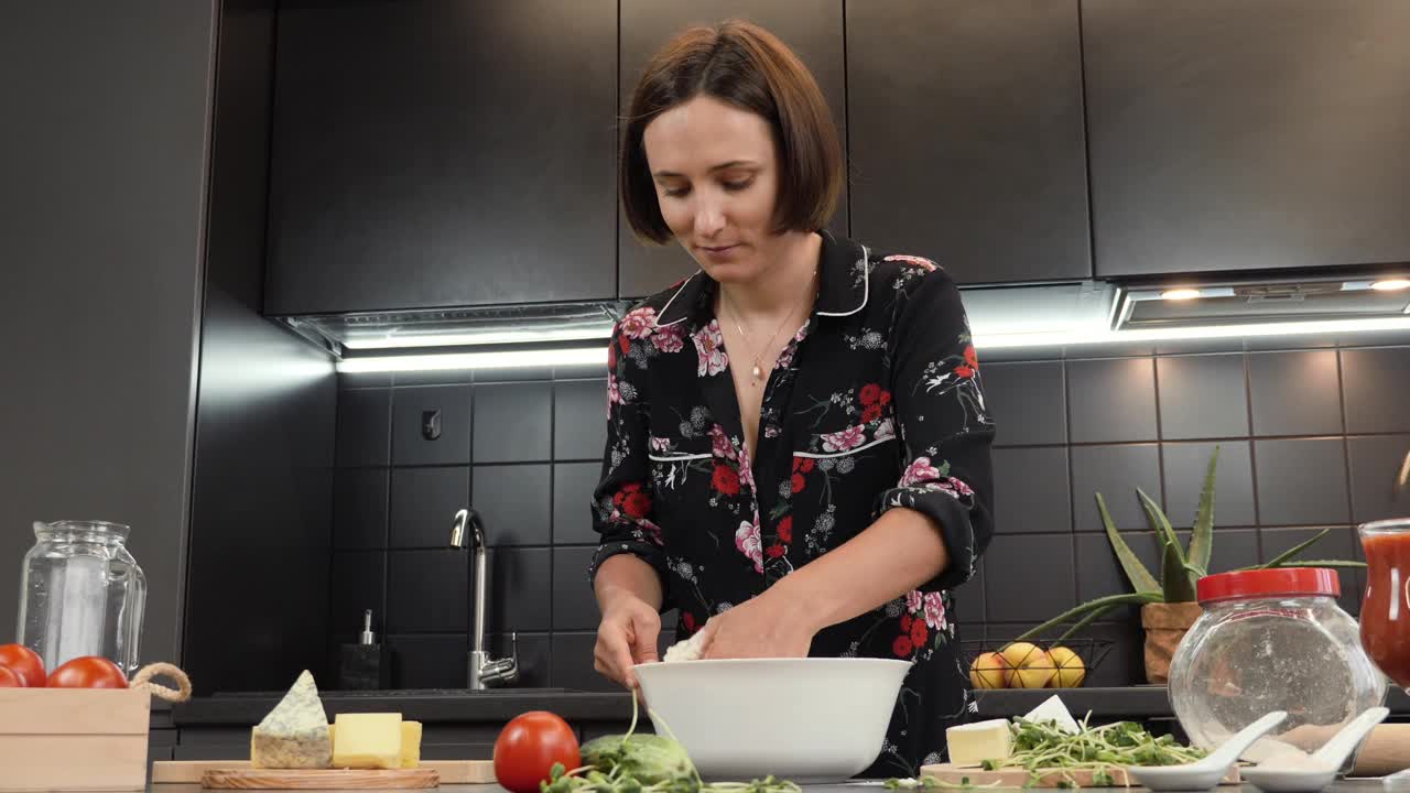 年轻开朗的女人在家庭厨房为家人做饭的肖像。女在碗里揉面团，准备披萨。手司康饼面团视频素材