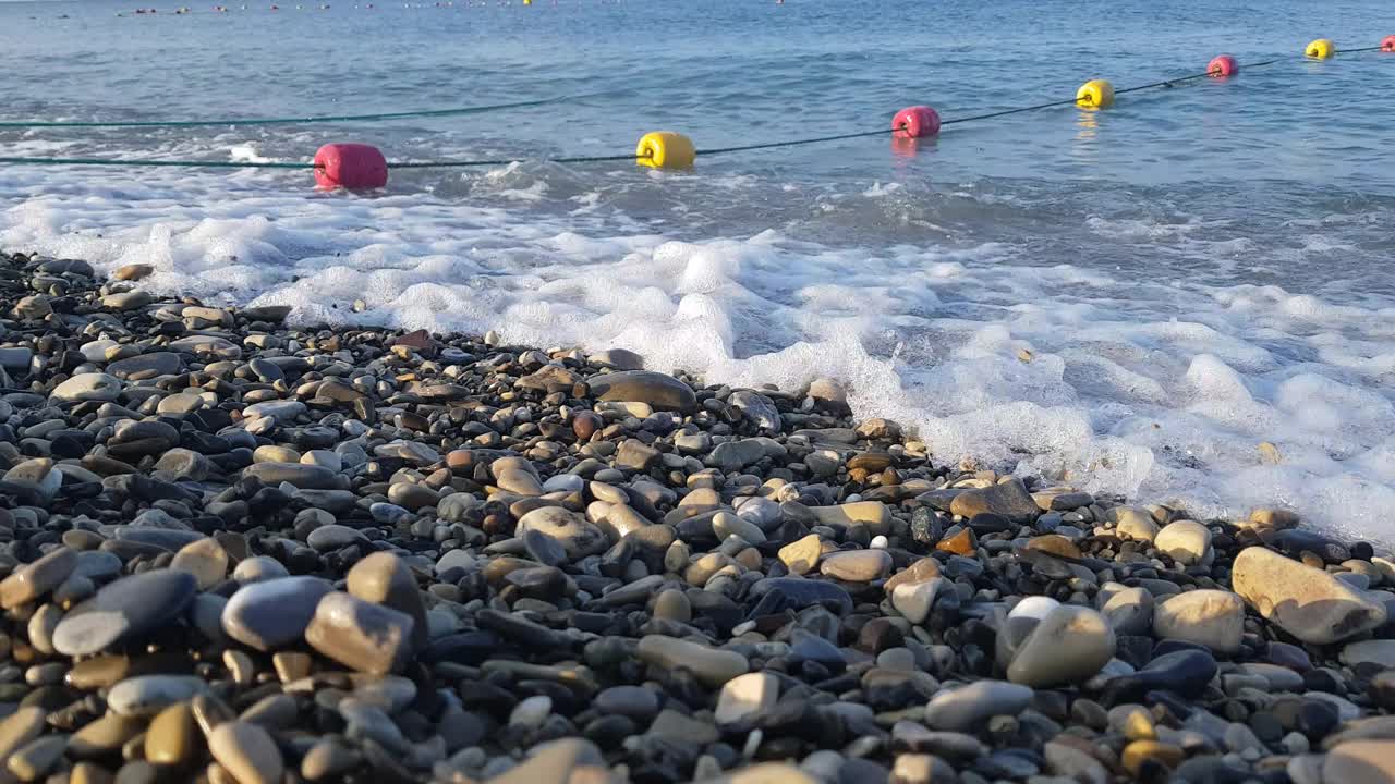 海滩上的卵石在岸边翻滚，海浪溅起水花。美丽的自然环境视频素材