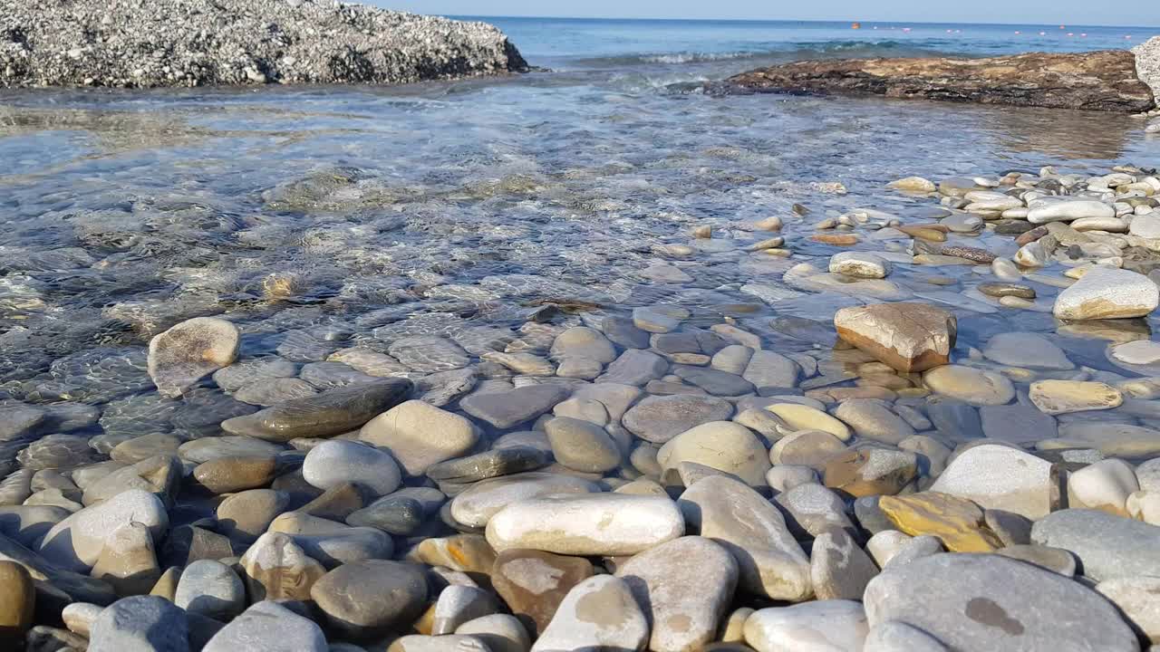 海滩上的卵石在岸边翻滚，海浪溅起水花。美丽的自然环境视频素材