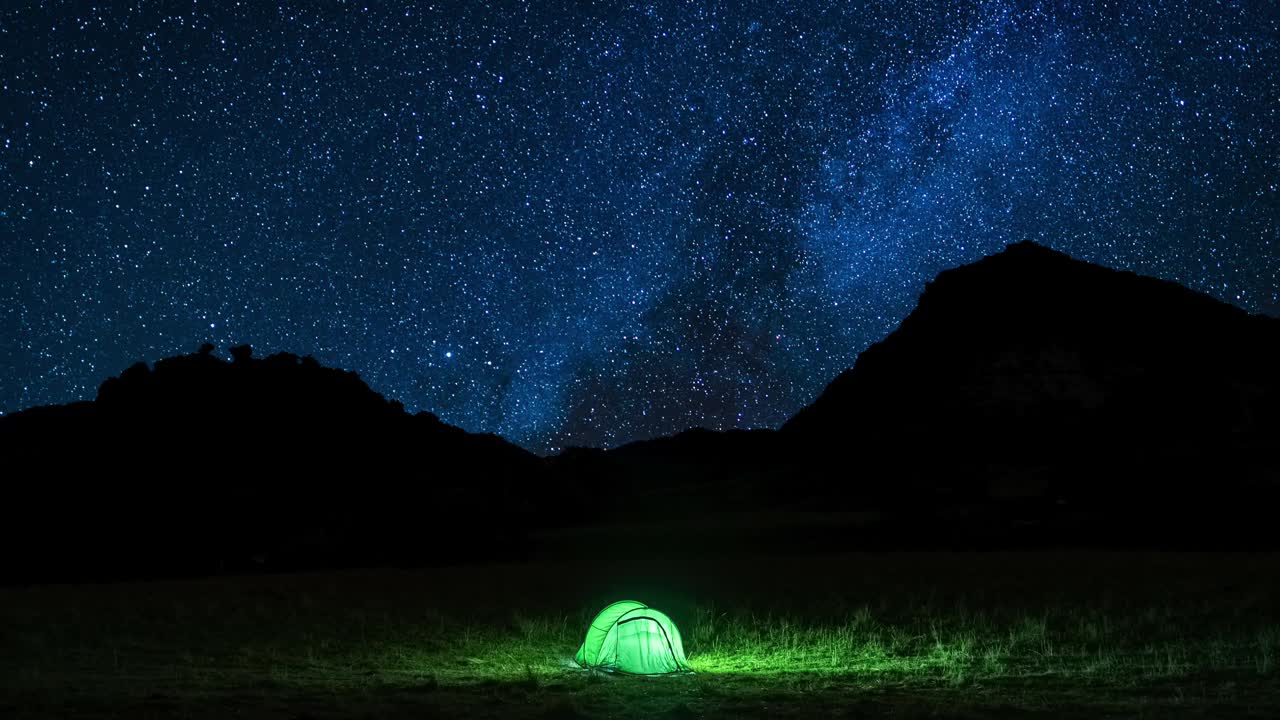 乡村的帐篷在繁星点点的夏夜下闪闪发光。帐篷被灯光照亮。在繁星点点的天空下露营。野生动物的概念。真正的户外探险。4 k间隔拍摄视频。视频素材