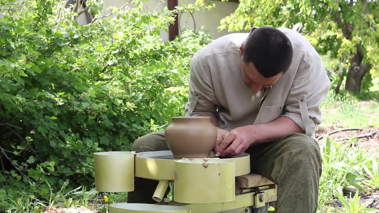 穿着工作衬衫的白人男性陶工在一个旋转的机器上制作一个大陶罐视频素材