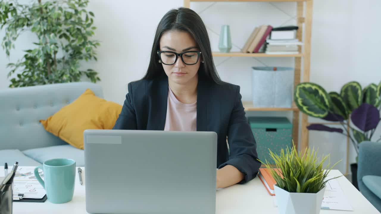 雄心勃勃的亚洲商业女性的肖像使用笔记本电脑打字，在公寓室内工作视频素材