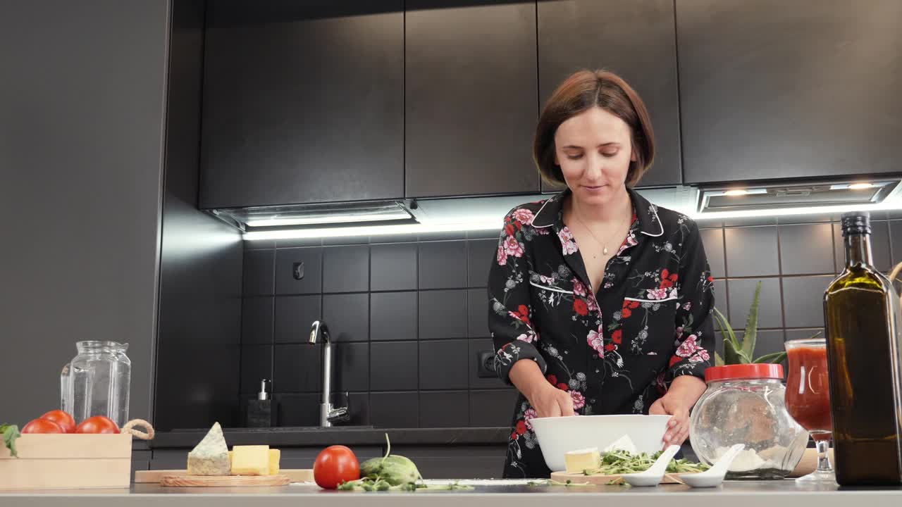 女人在现代化的厨房里做饭。年轻女性正在准备自制披萨，在碗里揉面团。烹饪过程。健康饮食的概念视频素材