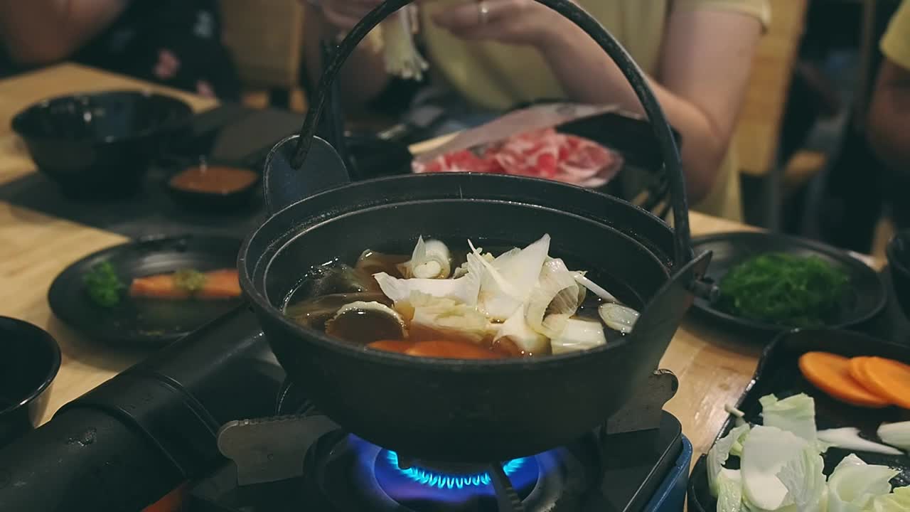 这名女子在一家日本餐馆里把金蘑菇放进涮锅里。和家人共进晚餐。视频素材