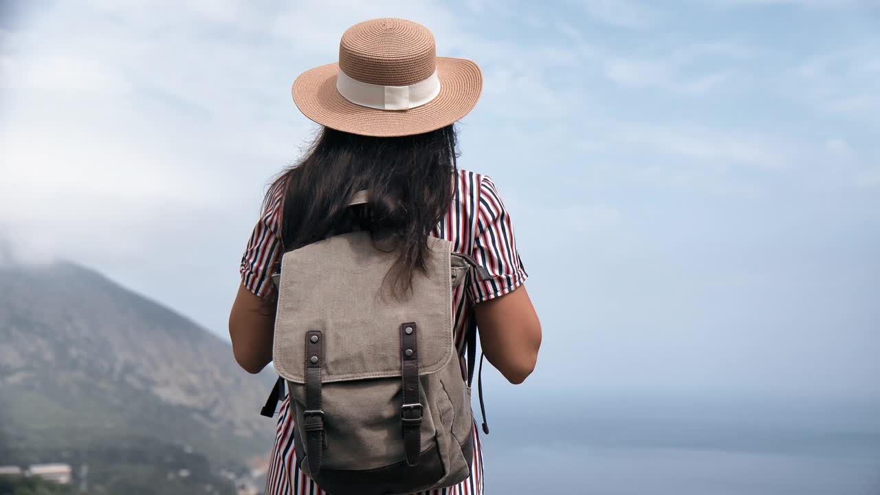 背景优雅的旅行女子草帽和背包欣赏惊人的海景山峰视频素材