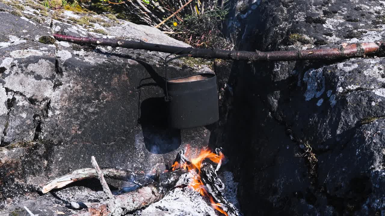 旅游水壶挂在燃烧的篝火在露营在远足。在野外用大锅烧饭。在野外生存。视频下载