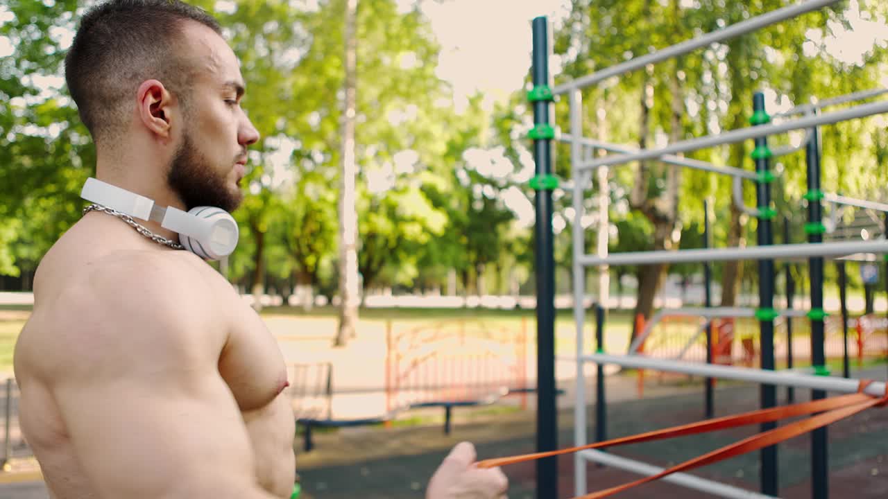 侧面的肌肉发达的胡子男人建立手臂和背部肌肉与松紧带训练视频素材