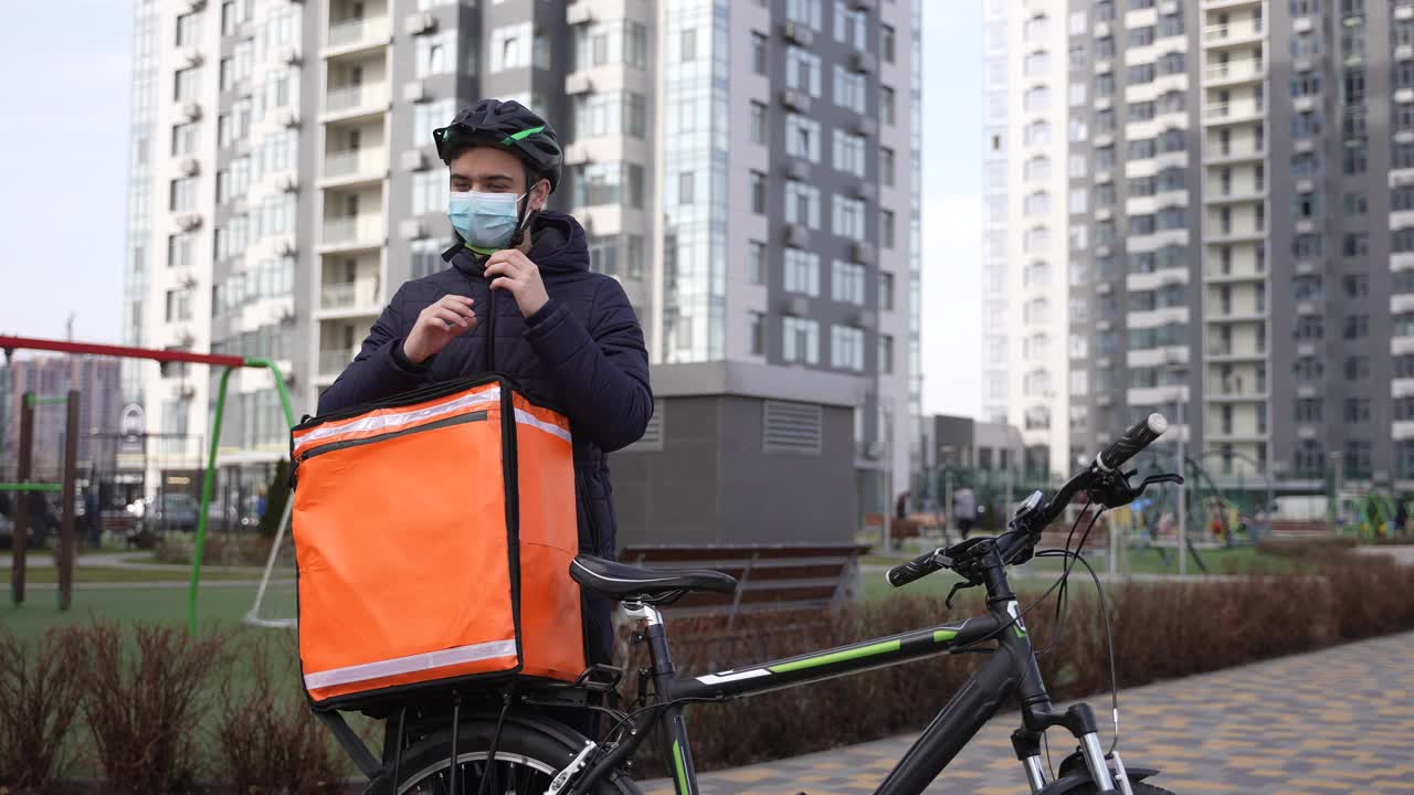 戴面具的食品快递员在休息时摘下头盔视频素材