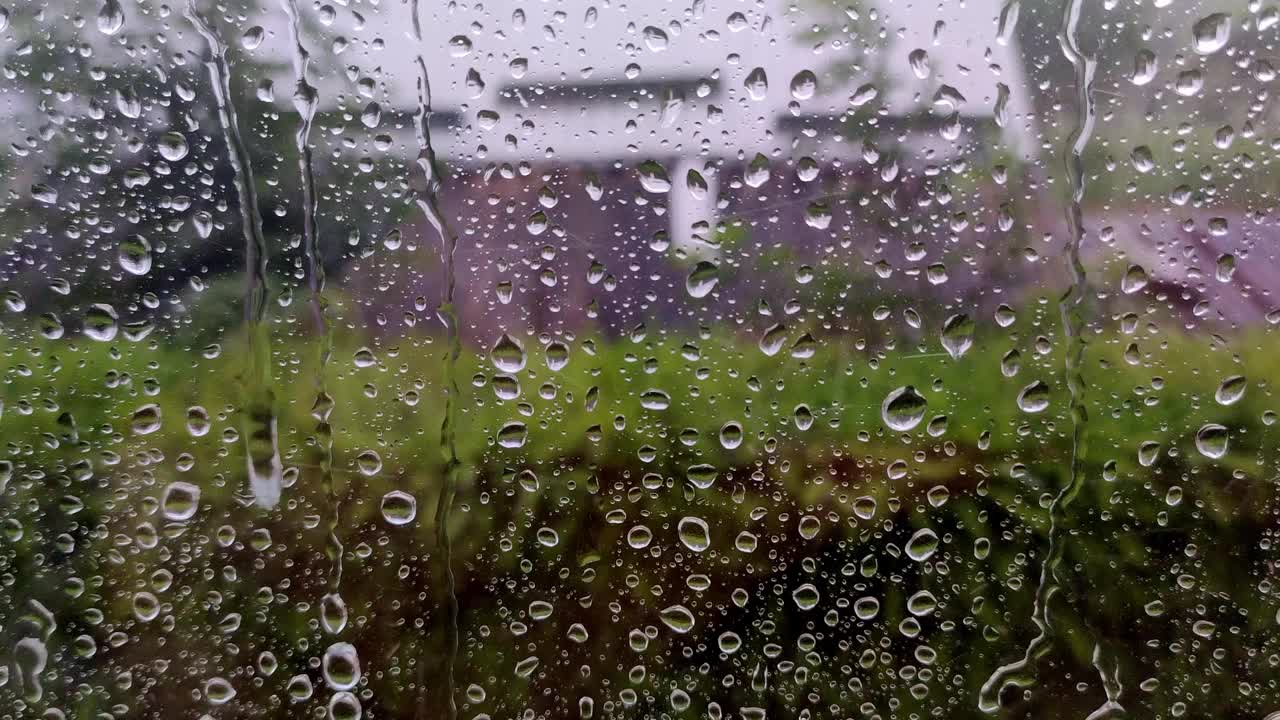 真正的雨滴滑落在家里的窗户玻璃上。大雨。玻璃上水滴的特写镜头。视频素材