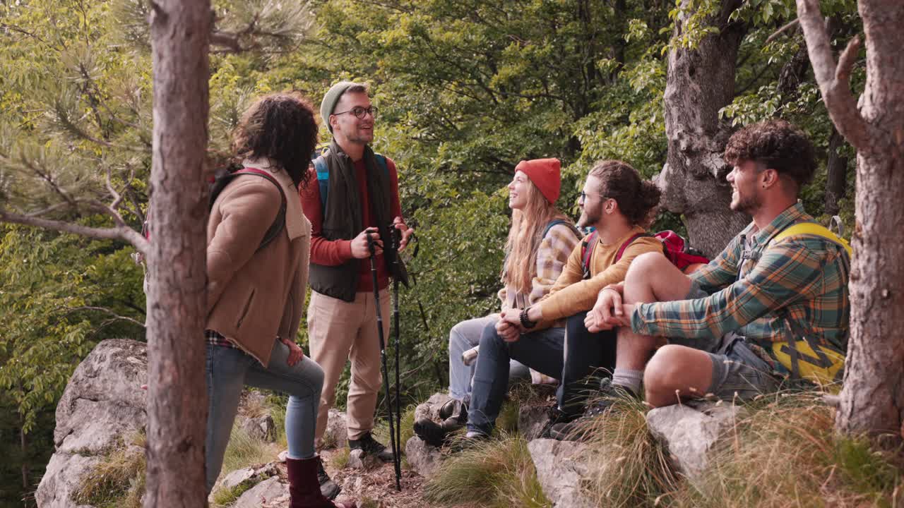 一群兴高采烈的年轻徒步旅行者坐在森林里聊天。视频素材