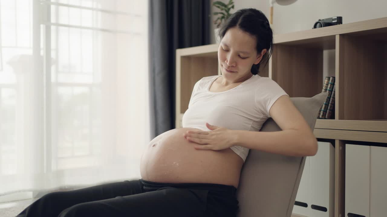 孕妇在家里把润肤霜涂在腹部视频素材